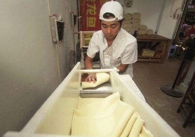 小蔡將面團(tuán)壓成面皮后，放在杠面器上切成面條